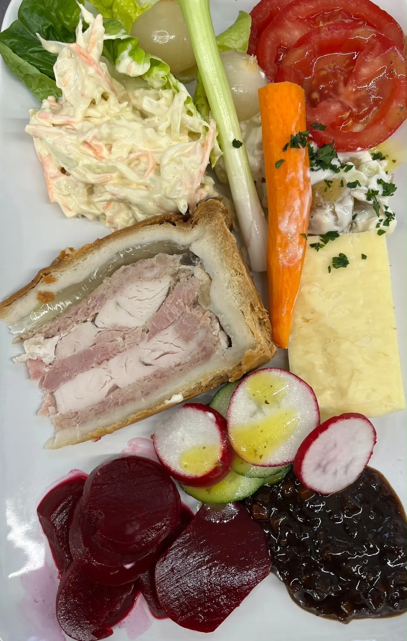 A ploughman's plate: a wedge of pork pie, mature cheddar, coleslaw, sliced tomato, radish, beetroot, celery, carrot and chutney