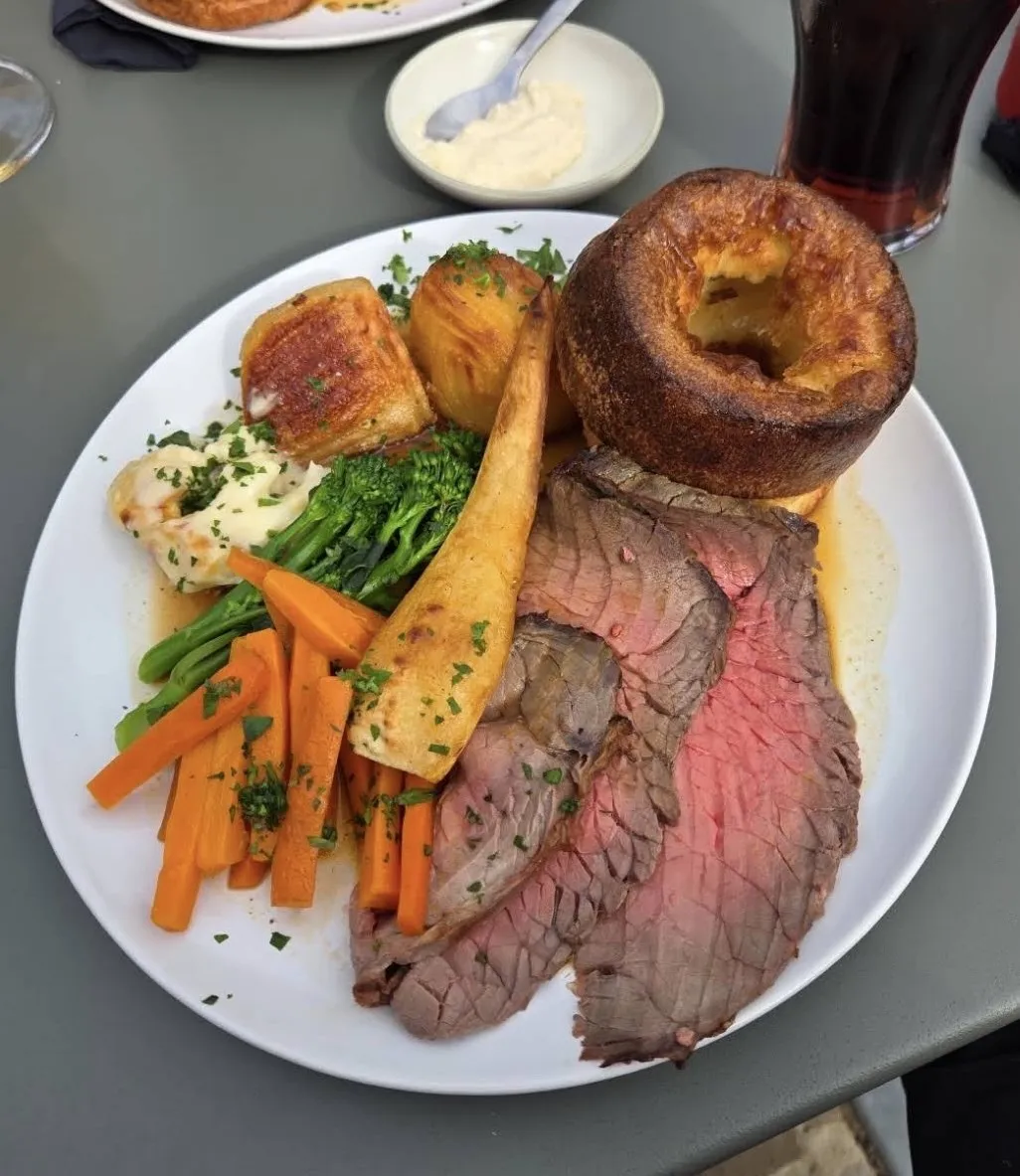 A Sunday roast: pink slices of roast beef with a tall Yorkshire pudding, crisp roast potatoes, a roast parsnip, carrots, tenderstem broccoli, cauliflower cheese and gravy, with horseradish on the side