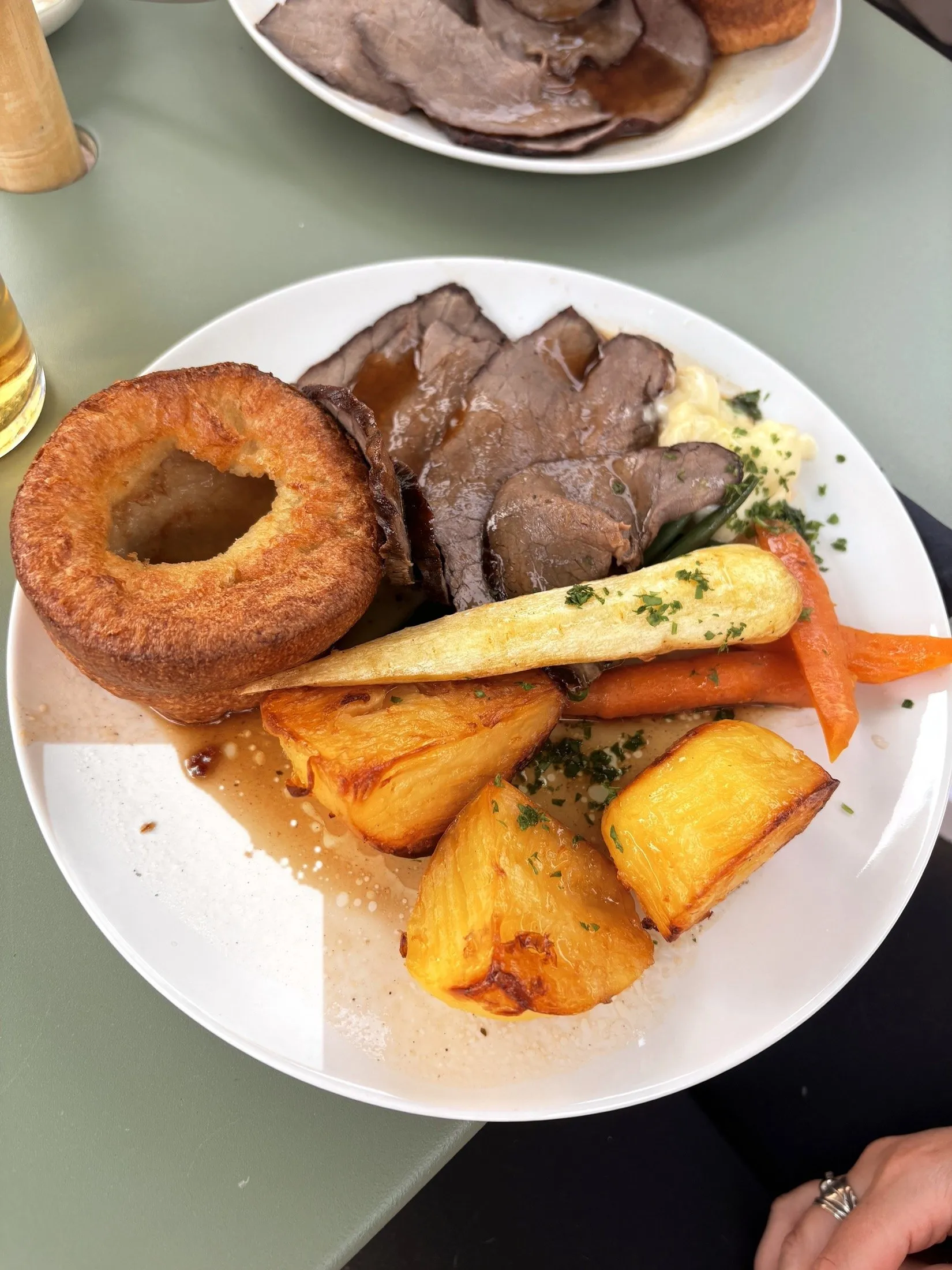 A Sunday roast: slices of roast beef with a Yorkshire pudding, roast potatoes, parsnip, carrots, green beans, cauliflower cheese and gravy
